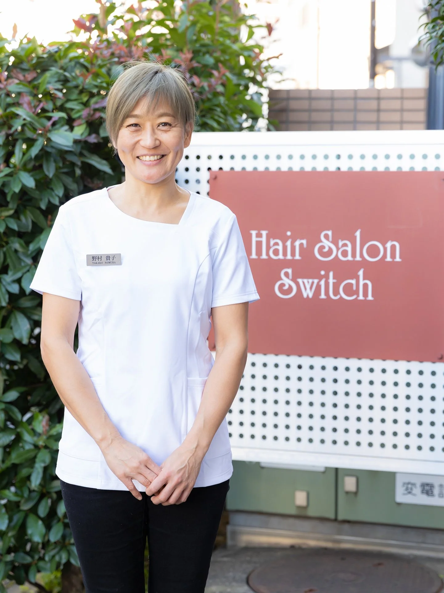 サロンの看板の前で微笑む店主の野村 貴子