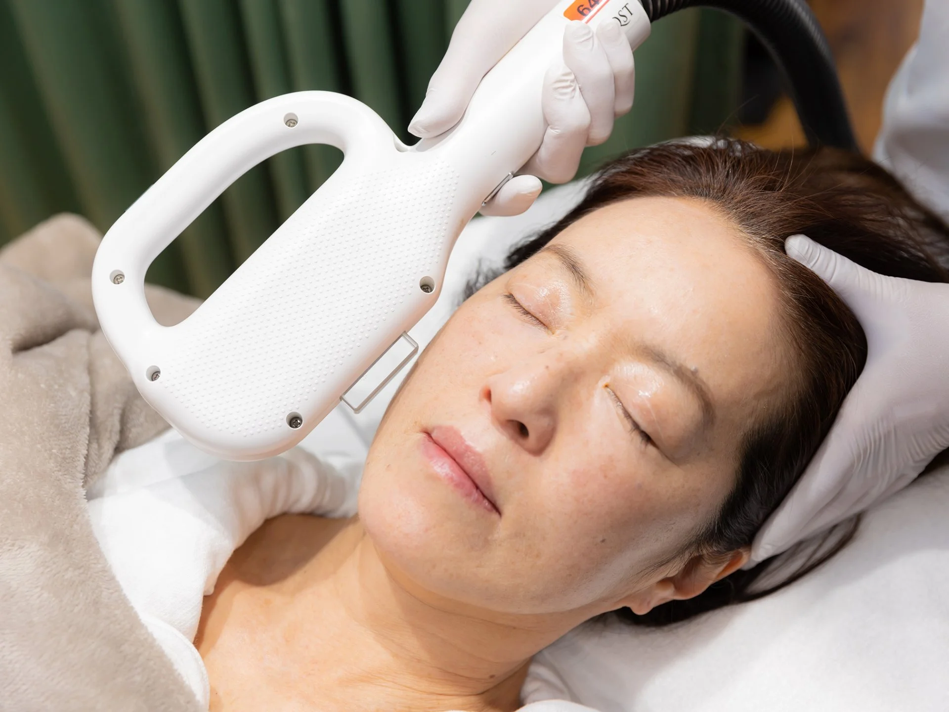 美顔器を使ったフェイシャルケアを受ける女性と、頭に手を添える施術者