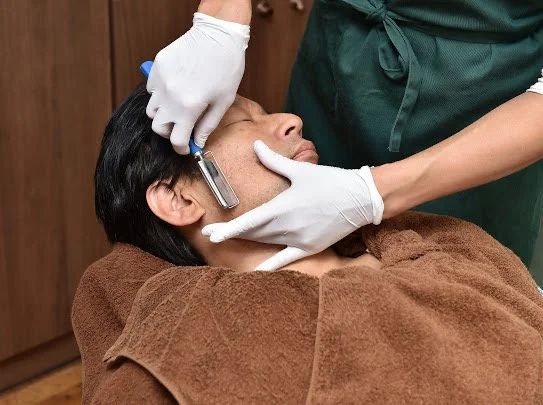 タオルをかけたお客様のお顔を剃刀でシェービングするスタッフの手元